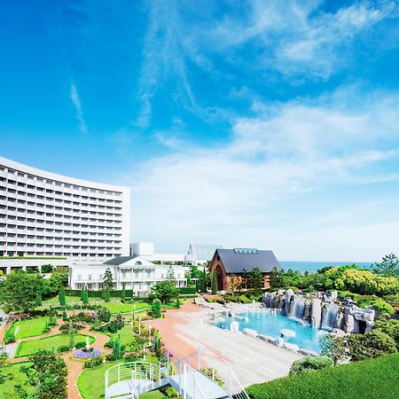 Sheraton Grande Tokyo Bay Hotel Urayasu Exterior photo The photo shows a luxurious hotel building with a modern architectural design, set against a bright blue sky. In the foreground, there is a beautifully landscaped garden featuring lush greenery, pathways, and seating areas. A sparkling swimming pool 